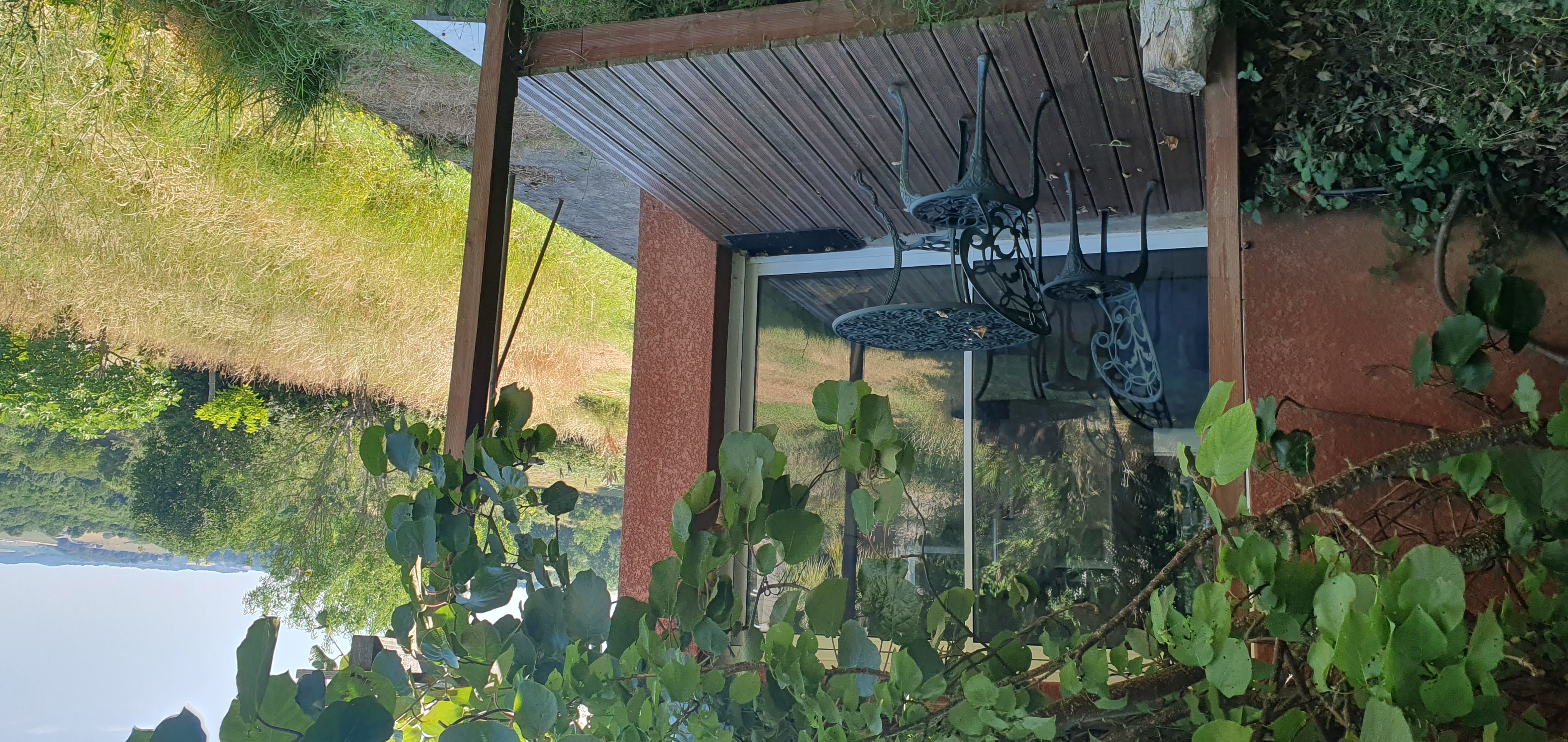 Terrasse ombragée avec une table et des chaises, ouverte sur le jardin et les collines.