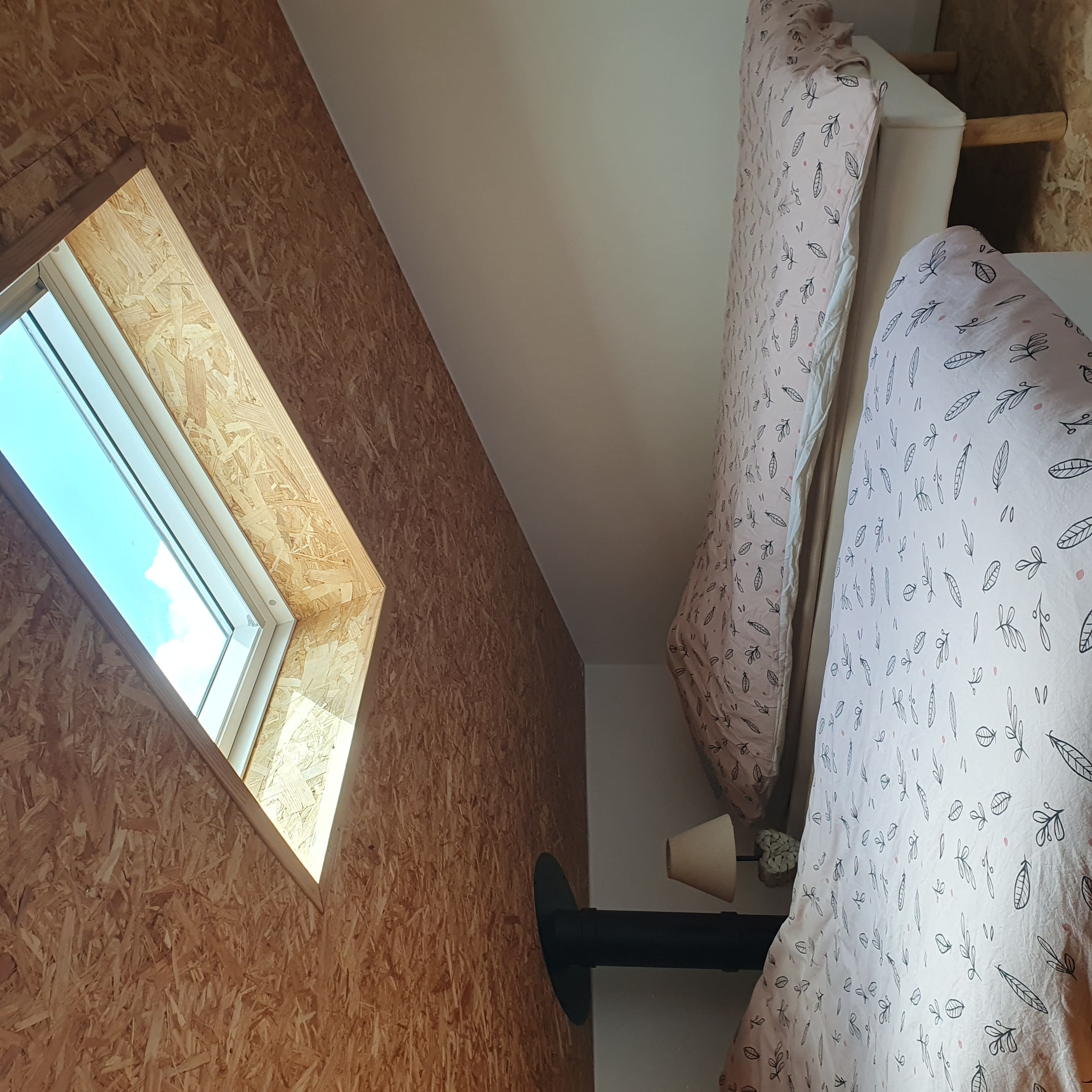 Deux lits aux couettes à motifs de feuilles sous une grande fenêtre de toit.